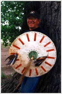 Butch Thunder Hawk standing before a tree holding circular hide shield.